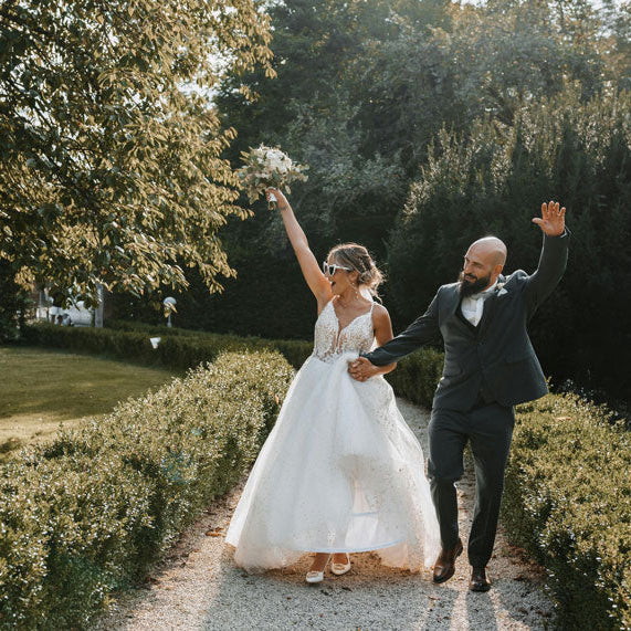 Arrivée des mariés, femme en grande robe blanche et homme en costume, les bras levés pour dire bonjour avec le sourire