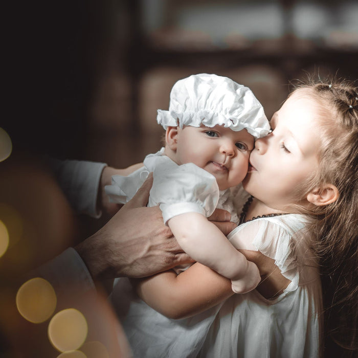 Jour de baptême, bébé dans les bras de sa sœur qui l'ambrasse fort