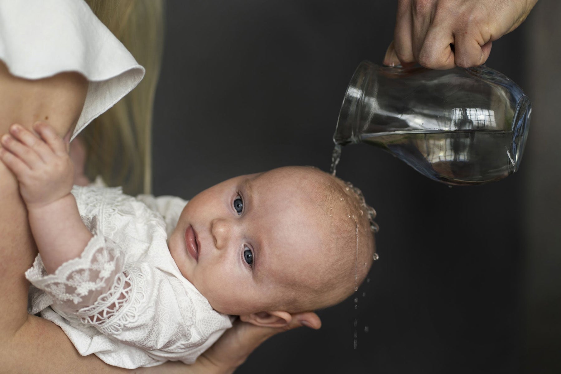 Bébé recevant le baptême. Eau sur la tête depuis les bras de sa marraine