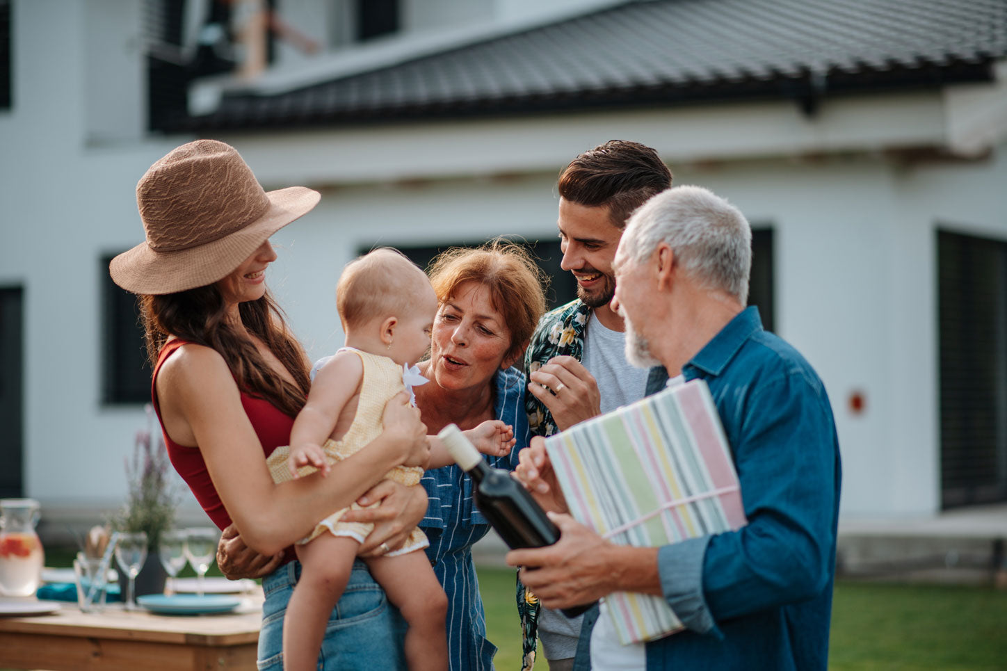 Famille autour de bébé dans les bars de maman. Papi porte le cadeau de baptême
