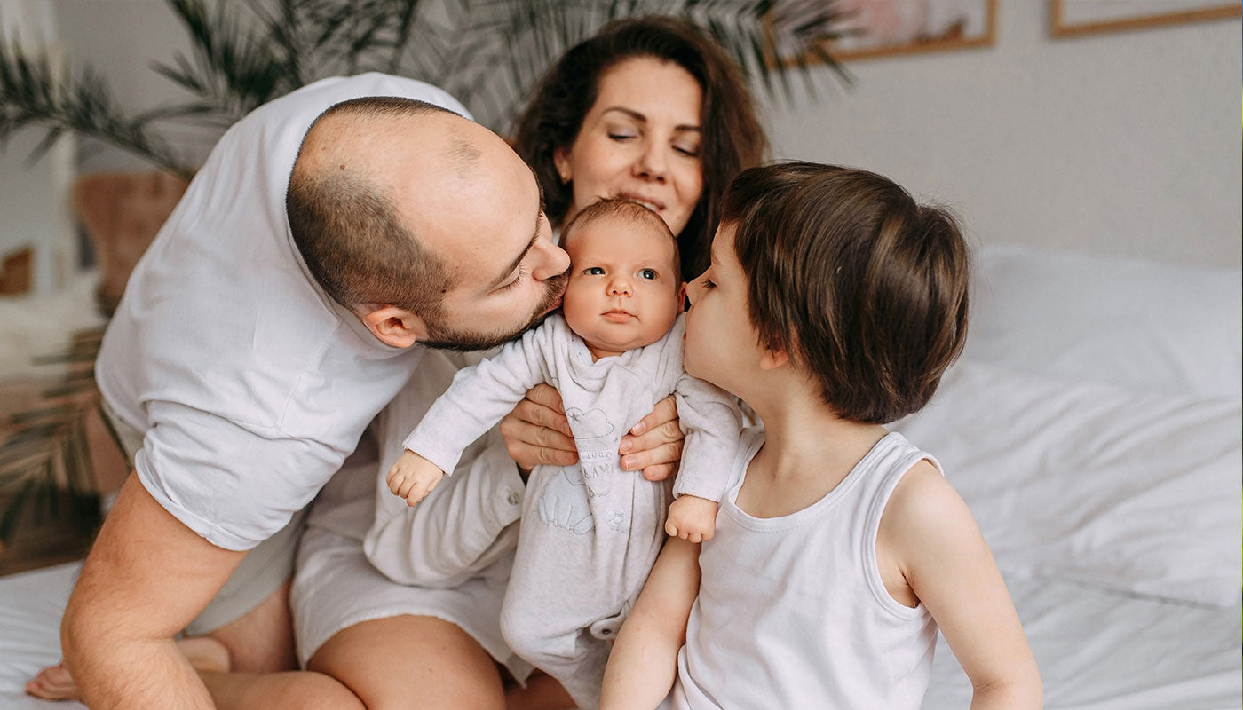 Famille avec bébé papa, maman et grand frère. Maman porte bébé, papa et grand frère lui font un bisou