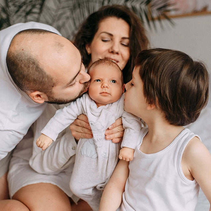 Famille avec bébé papa, maman et grand frère. Maman porte bébé, papa et grand frère lui font un bisou