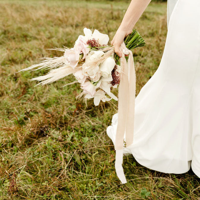 Mariée tenant son bouquet de fleurs, champêtre avec petite pampa. Jolie robe longue et blanche.