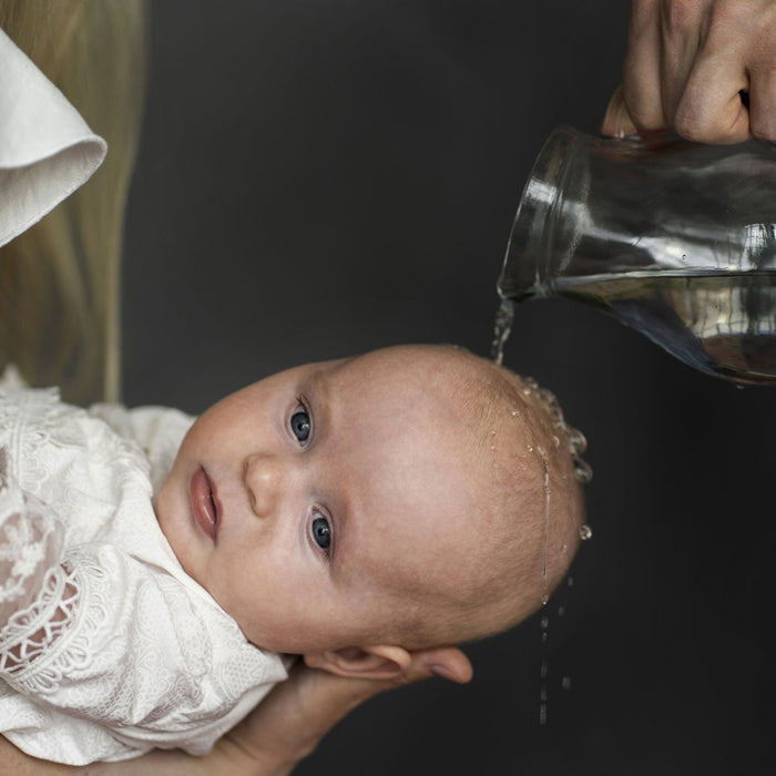 Bébé recevant le baptême. Eau sur la tête depuis les bras de sa marraine
