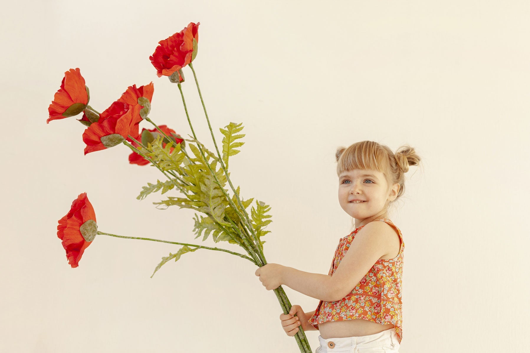 Petite fille portant un grand bouquet de fleurs, ce sont des coquelicots