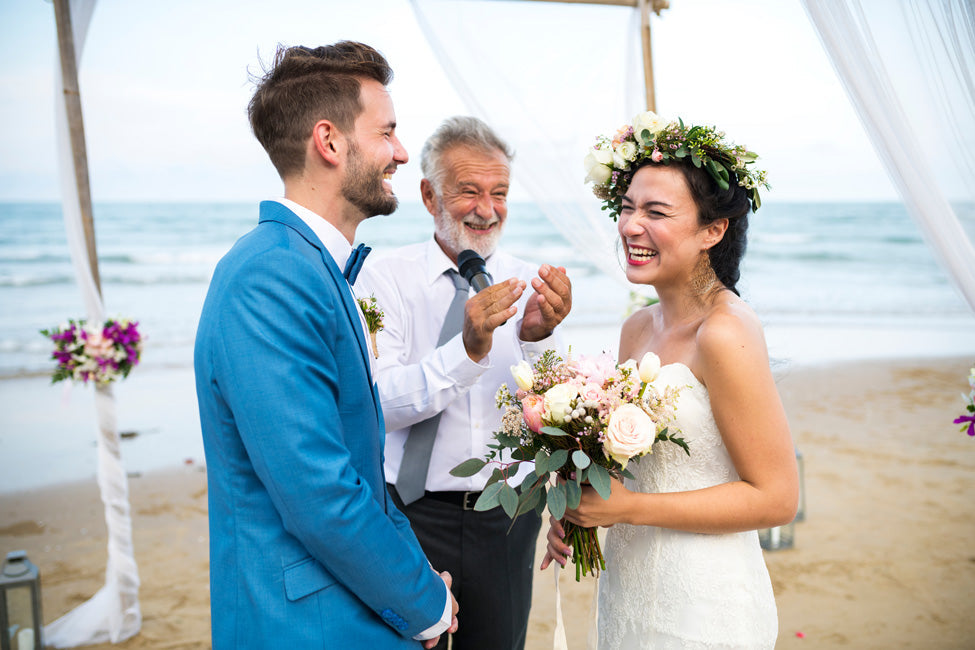 Mariés souriants sur la plage, félicités par le maitre de cérémonie