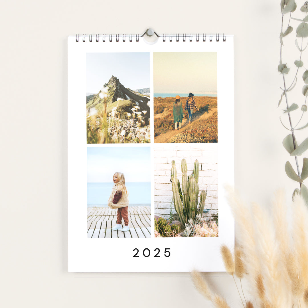 Wandkalender im A4-Format im Hochformat, der an einer Wand hängt und auf dem Deckblatt aufgeschlagen ist, das vier Reisefotos zeigt, darunter zwei Landschafts- und zwei Familienfotos, und unten die Jahreszahl 2025.